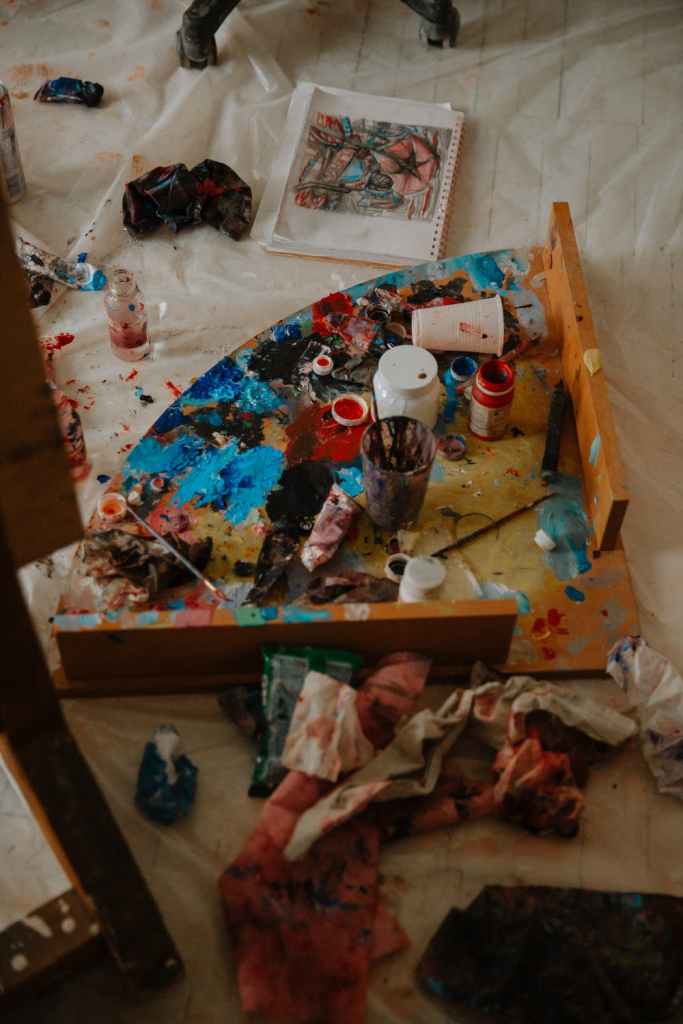 From above of paints on palette near supplies placed on oilcloth in art studio